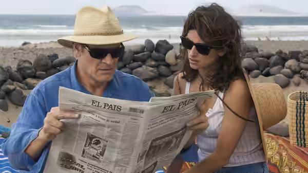 Mateo Blanco (Lluís Homar) reads a newspaper beside Lena (Penélope Cruz) on a beach