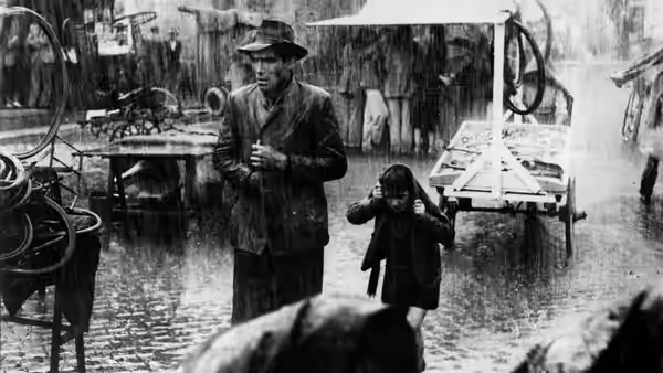 Antonio and Bruno stand in a rain-soaked street among bicycles