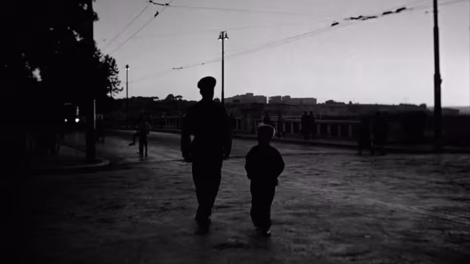 Man and boy walk together along a wide empty street at dusk