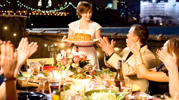 Julie Powell (Amy Adams) presents a cake as Eric Powell (Chris Messina) applauds at dinner