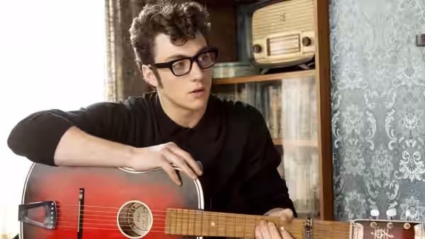John Lennon (Aaron Taylor-Johnson) holds an acoustic guitar beside a radio