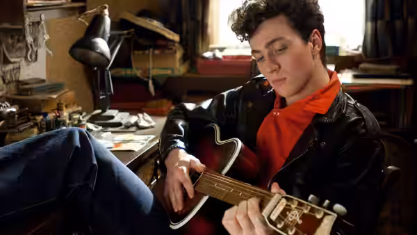 John Lennon (Aaron Taylor-Johnson) plays guitar in a cluttered room
