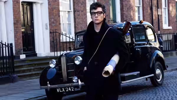 John Lennon (Aaron Taylor-Johnson) stands beside a black car outside a row of brick houses