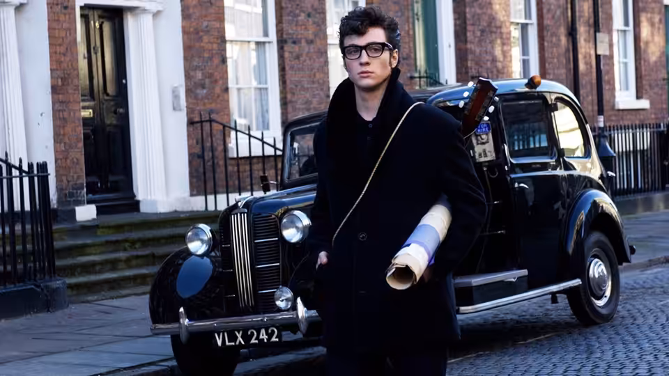 John Lennon (Aaron Taylor-Johnson) stands beside a black car outside a row of brick houses