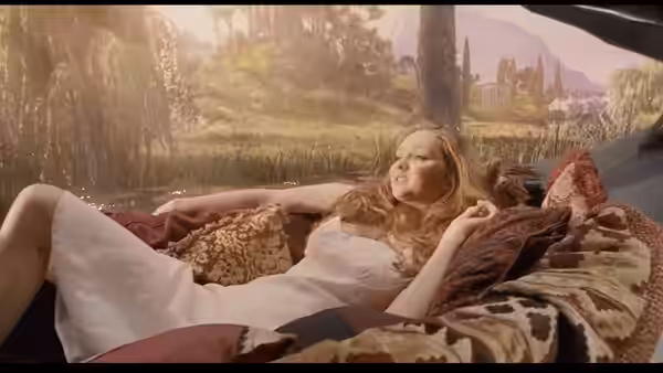 Valentina (Lily Cole) reclines on patterned cushions beside a fantastical landscape
