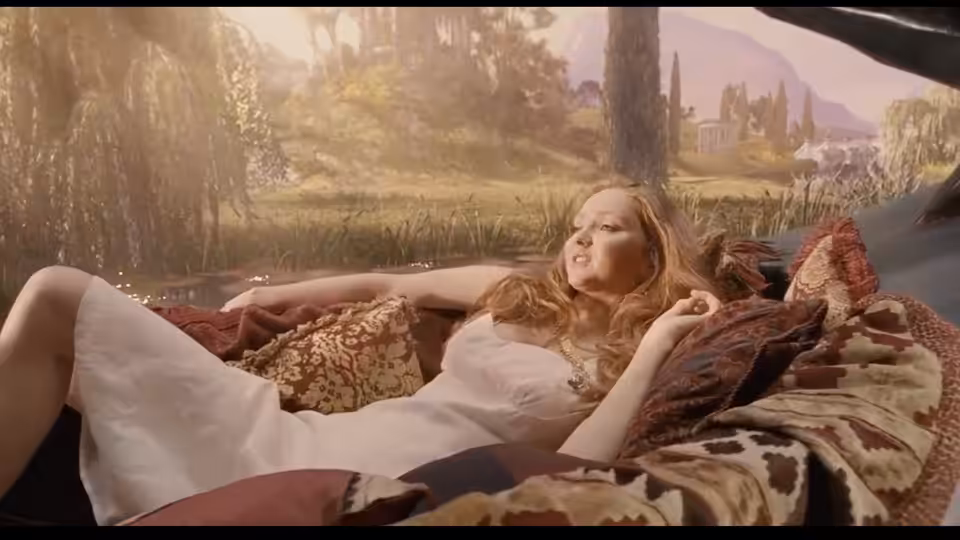 Valentina (Lily Cole) reclines on patterned cushions beside a fantastical landscape