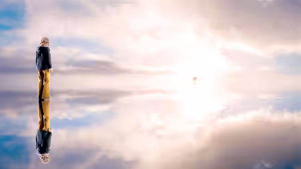 A girl stands above her reflection in a bright, cloudlike expanse