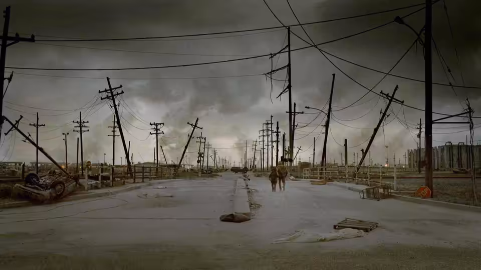The Father and Boy push their cart along a deserted road lined with leaning power poles