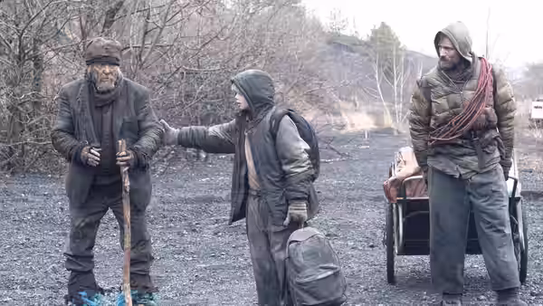 The Boy reaches toward Old Man Eli while the Father stands beside their cart