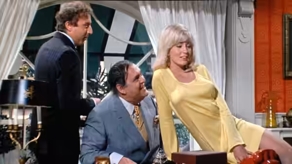 Ulla poses beside seated Max Bialystock as another man stands behind them