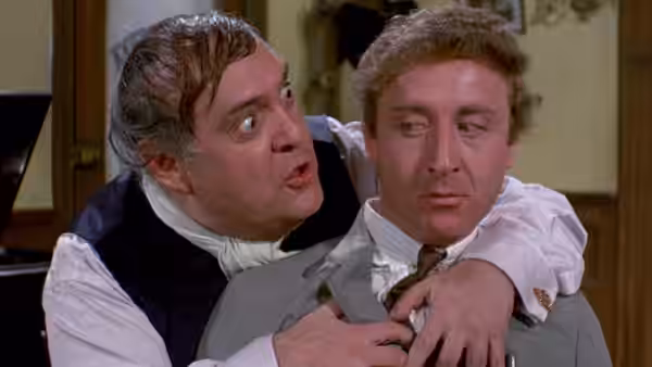 Franz Liebkind clutches Leo Bloom from behind as Leo looks sideways