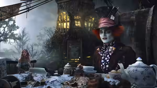 The Mad Hatter (Johnny Depp) sits at a crowded tea table as Alice watches