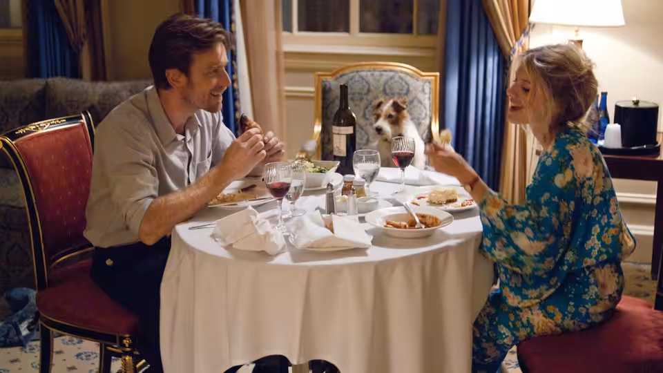 Oliver (Ewan McGregor) and Anna (Mélanie Laurent) share dinner across a table with their dog