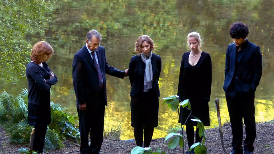 Five people stand beside a pond in a wooded clearing