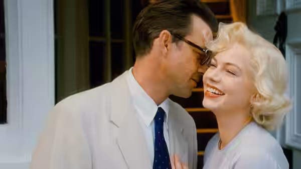 A blonde woman laughs beside a bespectacled man outside a doorway