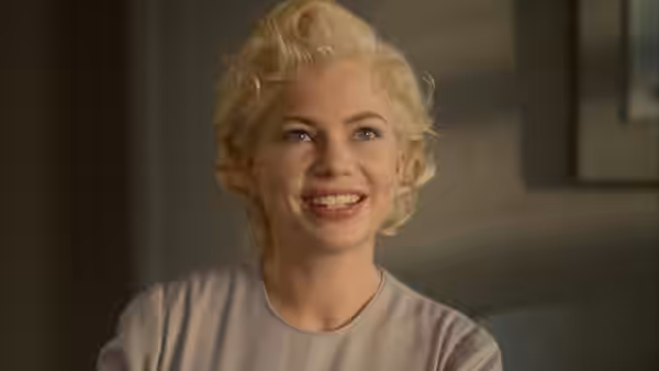 Marilyn Monroe (Michelle Williams) smiles in a pale blouse indoors