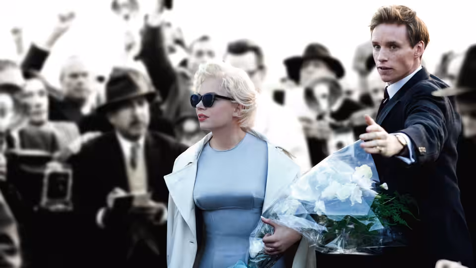 Marilyn Monroe (Michelle Williams) walks with Colin Clark (Eddie Redmayne) through a crowd of photographers