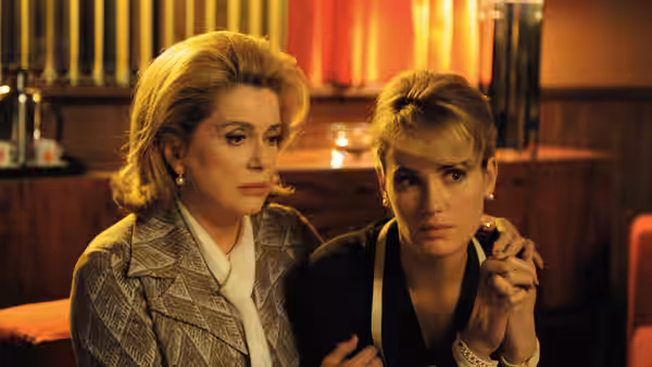 Suzanne Pujol (Catherine Deneuve) holds a younger woman close in a warmly lit room
