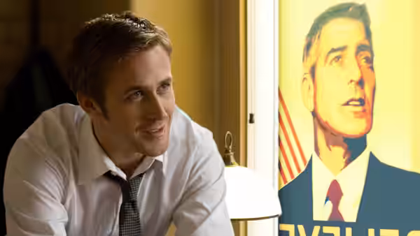 Stephen Meyers (Ryan Gosling) leans forward beside a campaign poster of Mike Morris
