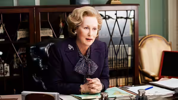 Margaret Thatcher (Meryl Streep) sits at her desk in an office, hands clasped over papers