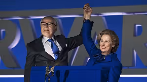 Margaret Thatcher (Meryl Streep) raises a clasped hand beside a suited man at a campaign podium