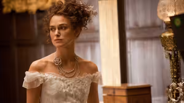 Anna Karenina (Keira Knightley) stands in an off-the-shoulder white gown beside a mirror