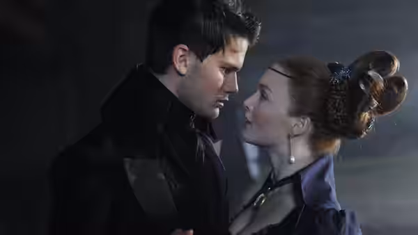 Pip (Jeremy Irvine) and Estella (Holliday Grainger) gaze at each other in a dim room