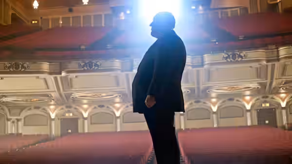 A silhouetted man stands before the empty seats of an ornate theater