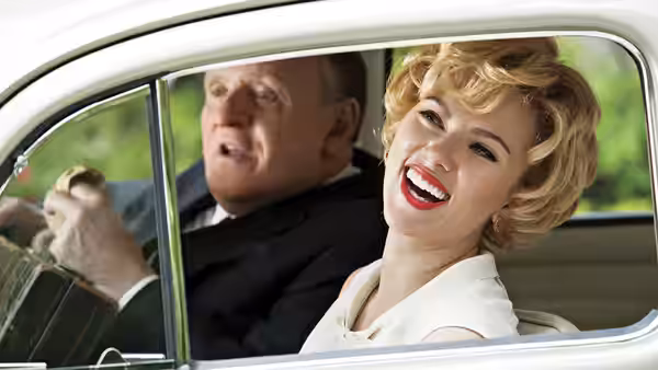 Alfred Hitchcock (Anthony Hopkins) drives while Janet Leigh (Scarlett Johansson) smiles beside him