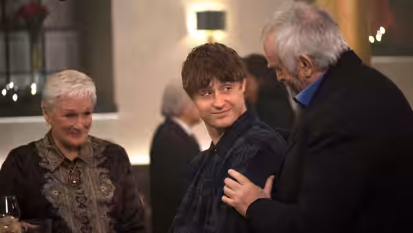 Joe Castleman (Jonathan Pryce) rests a hand on David Castleman’s shoulder as Joan watches
