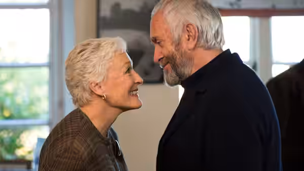 Joan Castleman (Glenn Close) and Joe Castleman (Jonathan Pryce) smile at each other indoors