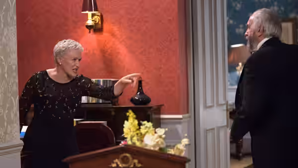 Joan Castleman (Glenn Close) gestures toward Joe Castleman (Jonathan Pryce) in a sitting room