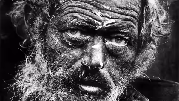 A bearded man with a weathered face looks directly ahead