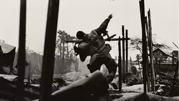 A man carries another through the rubble of a war-damaged village