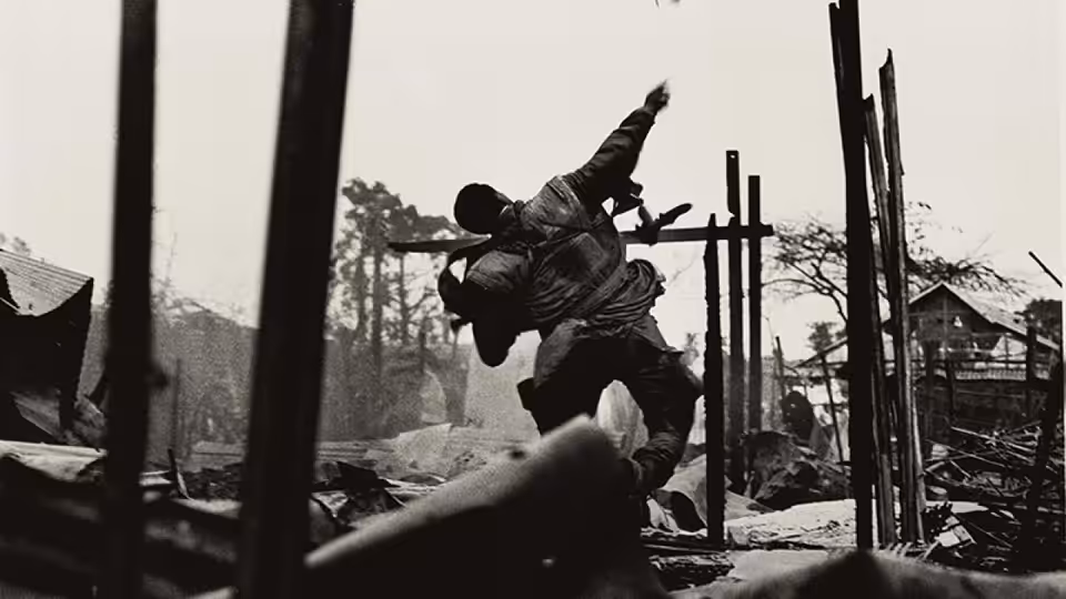 A man carries another through the rubble of a war-damaged village
