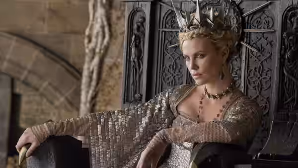 Queen Ravenna (Charlize Theron) sits crowned before an ornate throne