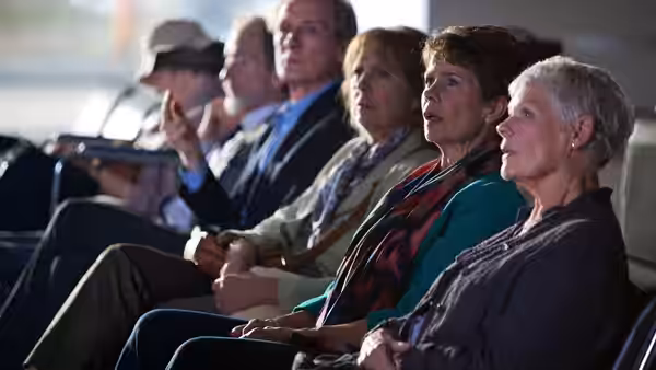 Hotel guests sit in a row watching something offscreen