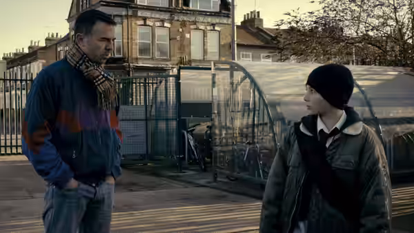 Bill (Charlie Creed-Miles) talks with Dean (Will Poulter) beside a fenced housing estate