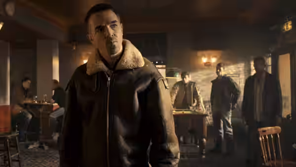 Bill (Charlie Creed-Miles) stands in a pub as several men gather behind him