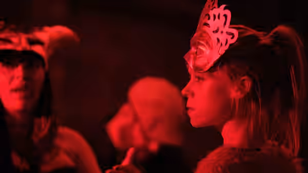 Kelly (Antonia Campbell-Hughes) watches the crowd in a decorative mask under red lights