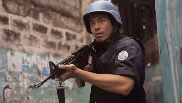 Douglas Ong (John Arcilla), wearing a security uniform and helmet, aims a rifle in an alley