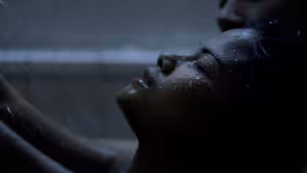 A woman reclines under running water as another person supports her head