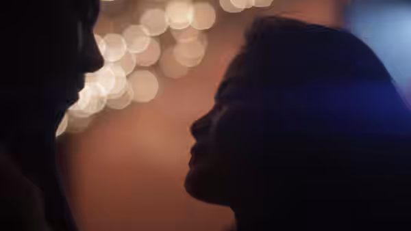 A man and woman face each other in silhouette against blurred city lights