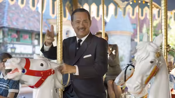 Walt Disney (Tom Hanks) smiles and waves while riding a carousel horse