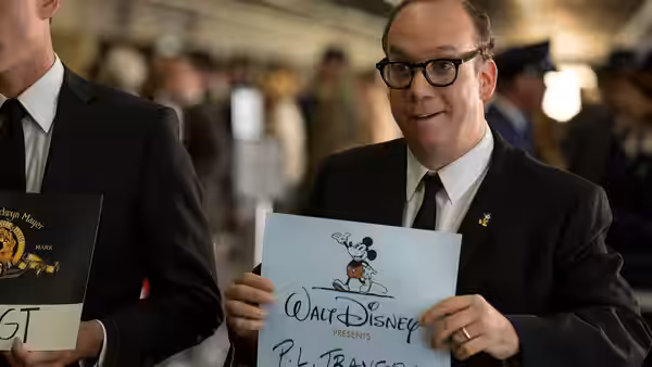 A bespectacled man holds up a Walt Disney Productions presentation board at a gathering