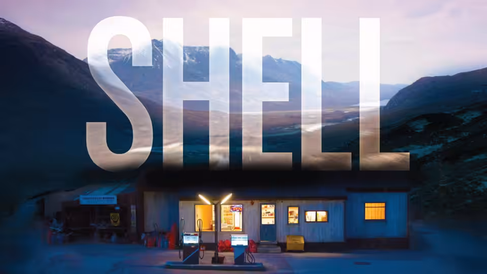 A small roadside petrol station glows beneath mountains at dusk