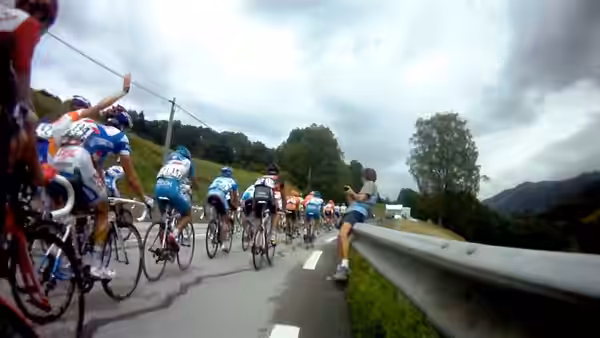 A peloton of cyclists races along a mountain road past a spectator