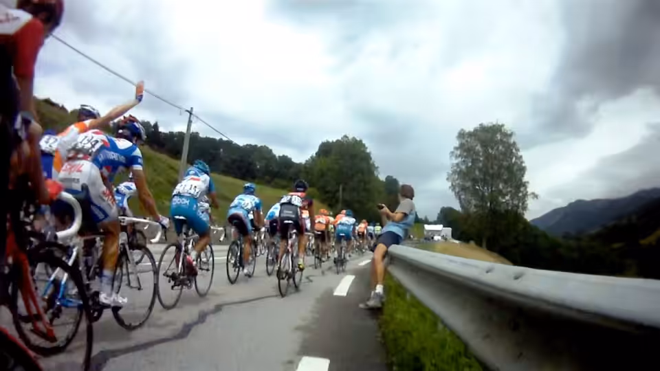 A peloton of cyclists races along a mountain road past a spectator