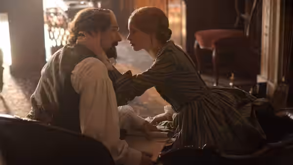 Charles Dickens (Ralph Fiennes) leans close as Nelly Ternan (Felicity Jones) reaches toward him indoors