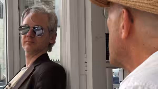 Julian Assange in sunglasses faces a man beside a window
